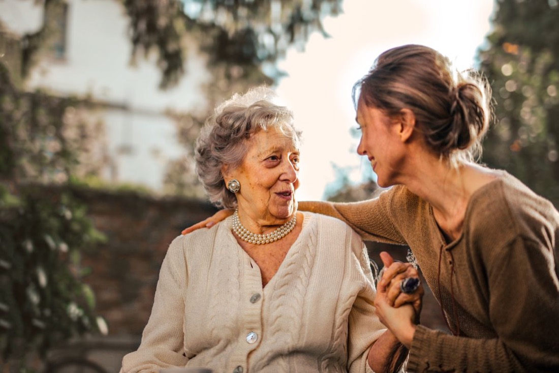An adult daughter laughing with her mother in the garden of a senior living community