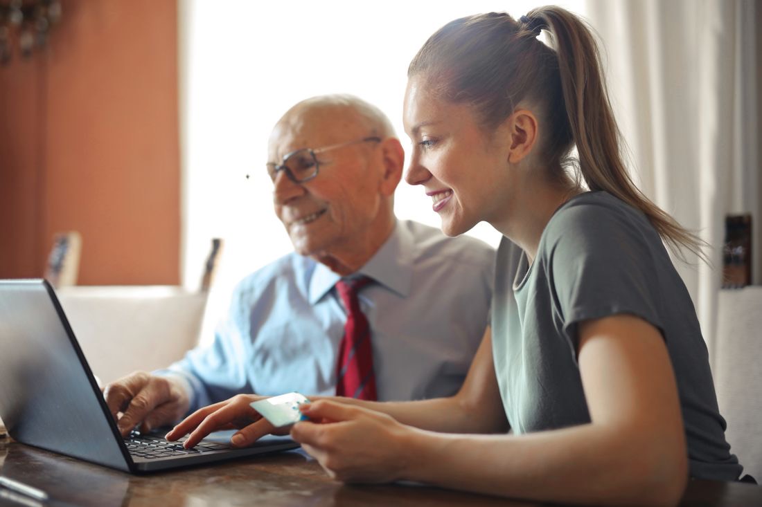 A granddaughter and grandfather smiling as they work through options on a laptop together