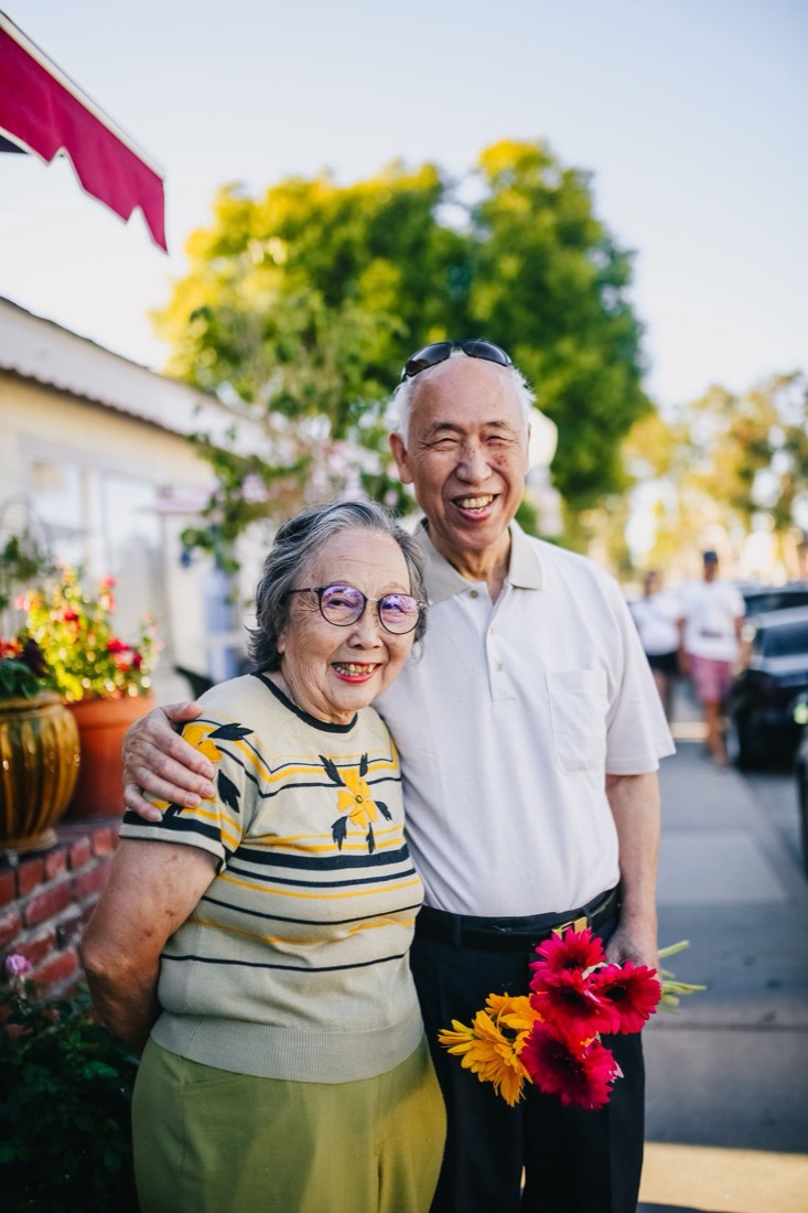 A joyful older couple out on a sunny sidewalk holding fresh flowers