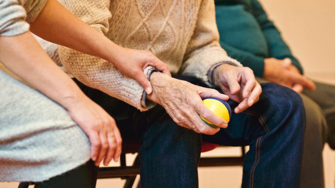 A caregiver's hand gently supporting an older man's arm during an activity