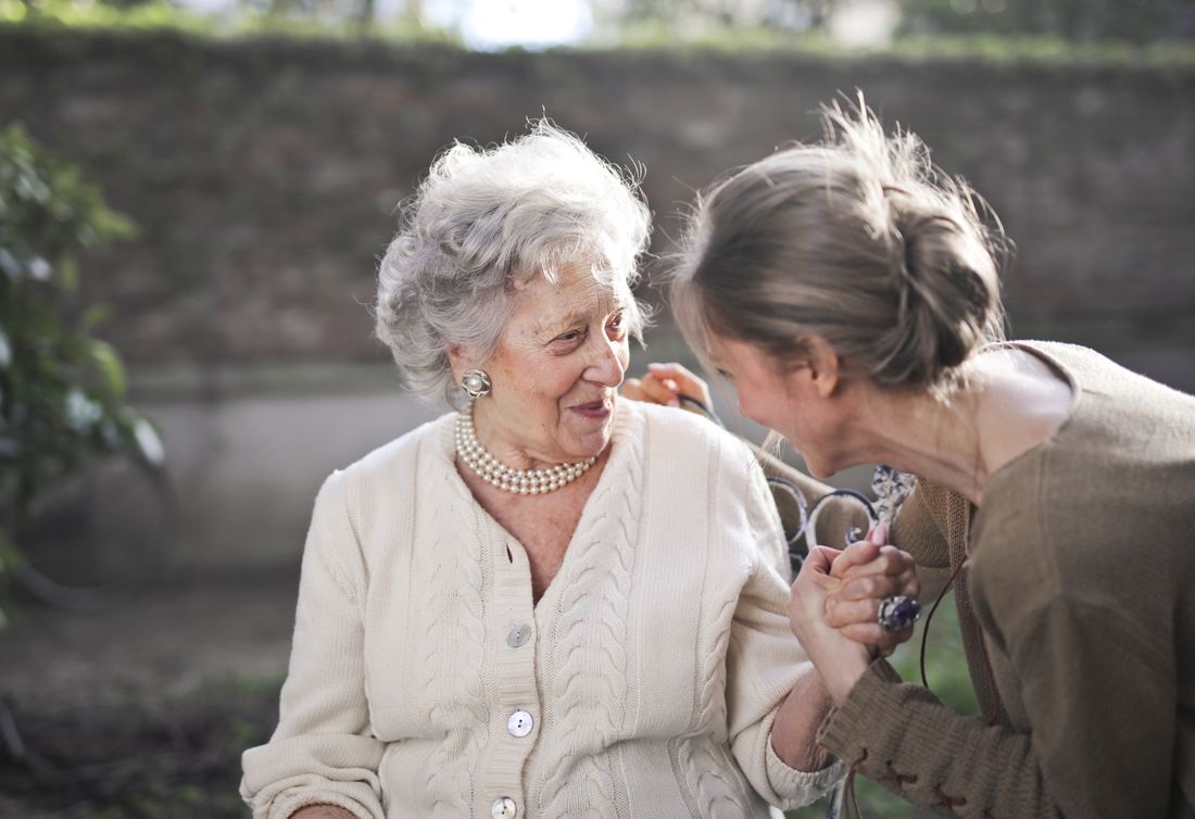 An adult daughter and her mother laughing together, hands clasped
